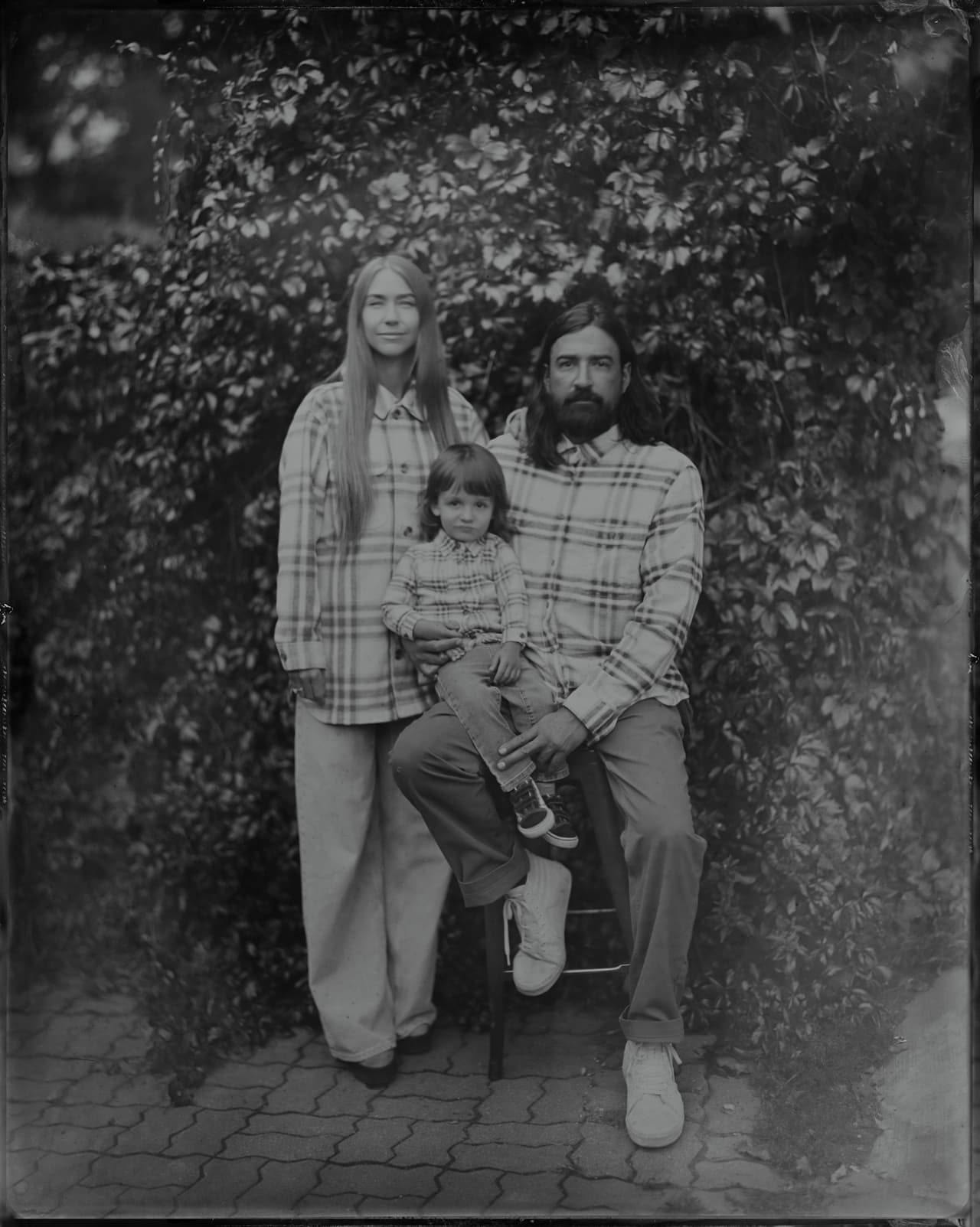 Father holding young child with mother beside them, posed against foliage in tintype portrait