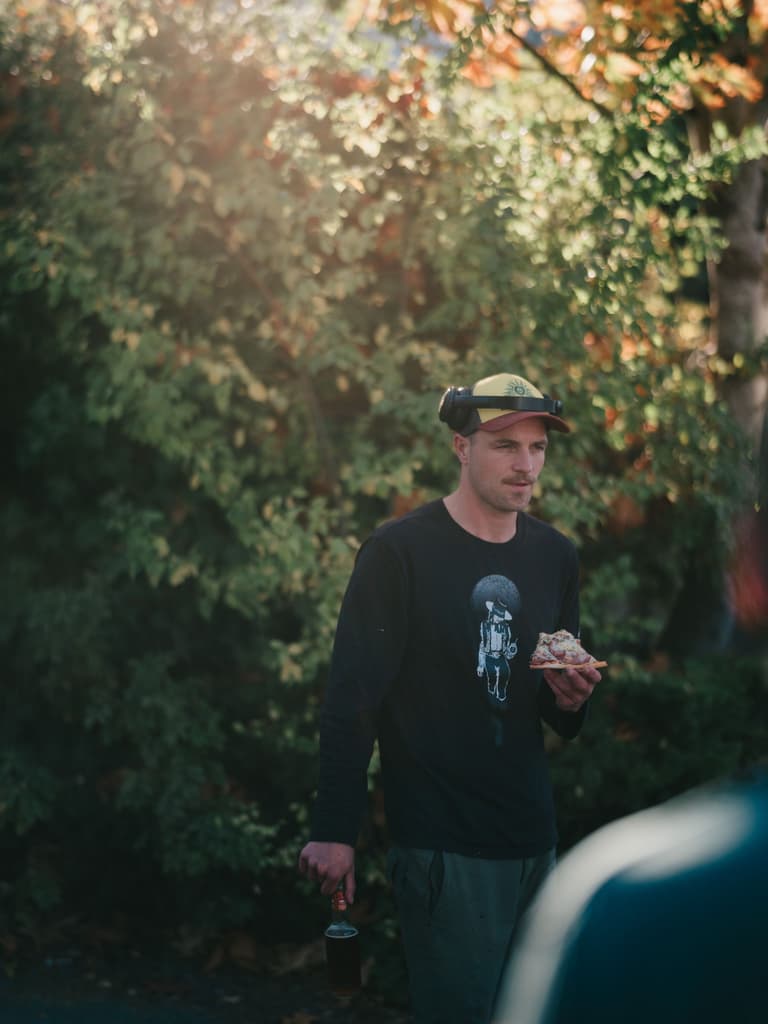 Person in black shirt and cap holds a drink before an ivy-covered wall at the Salt Spring Island Convergence Festival