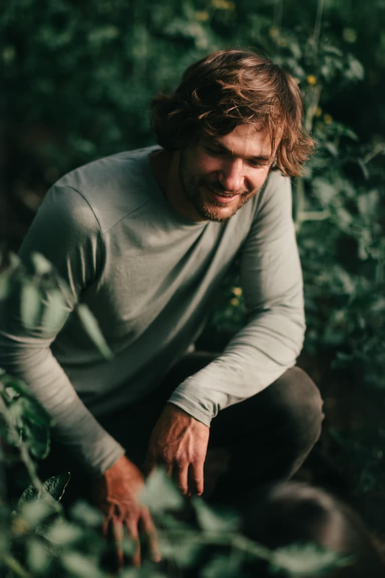 A smiling grower crouched among green plants on a Salt Spring Island farm