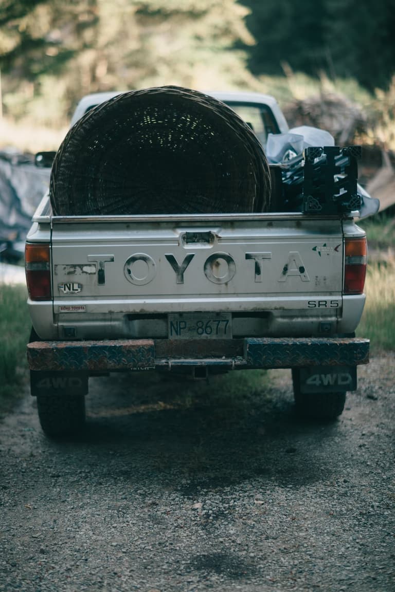An old pickup truck with a large basket in the back, parked on a farm track