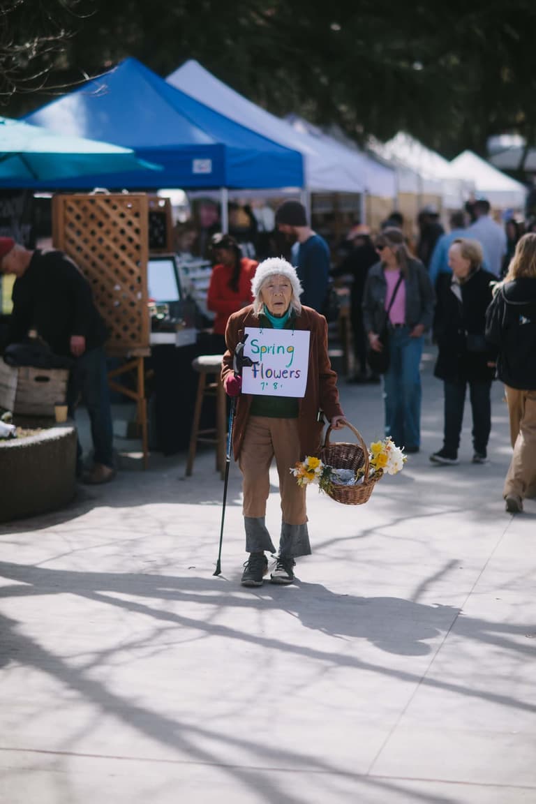 An older woman with a cane and a basket of flowers walking through the Saturday market on Salt Spring Island