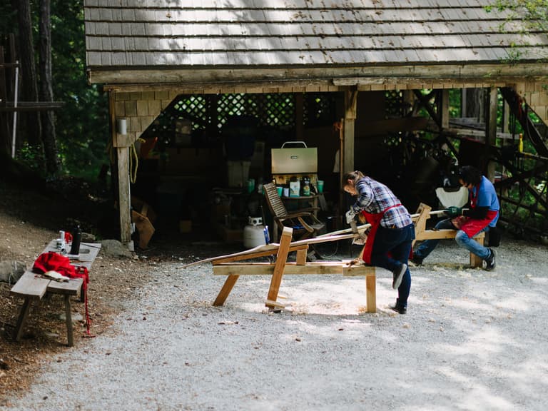 Participants working at shave horses under the pavilion during a bow making workshop