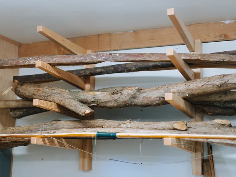 Split bow staves seasoning on wooden brackets high on the workshop wall