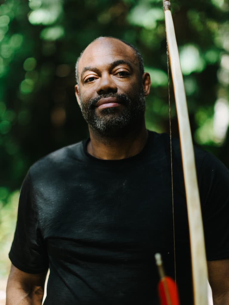 Bowyer Christopher Applewhaite standing among the trees with a strung wooden bow