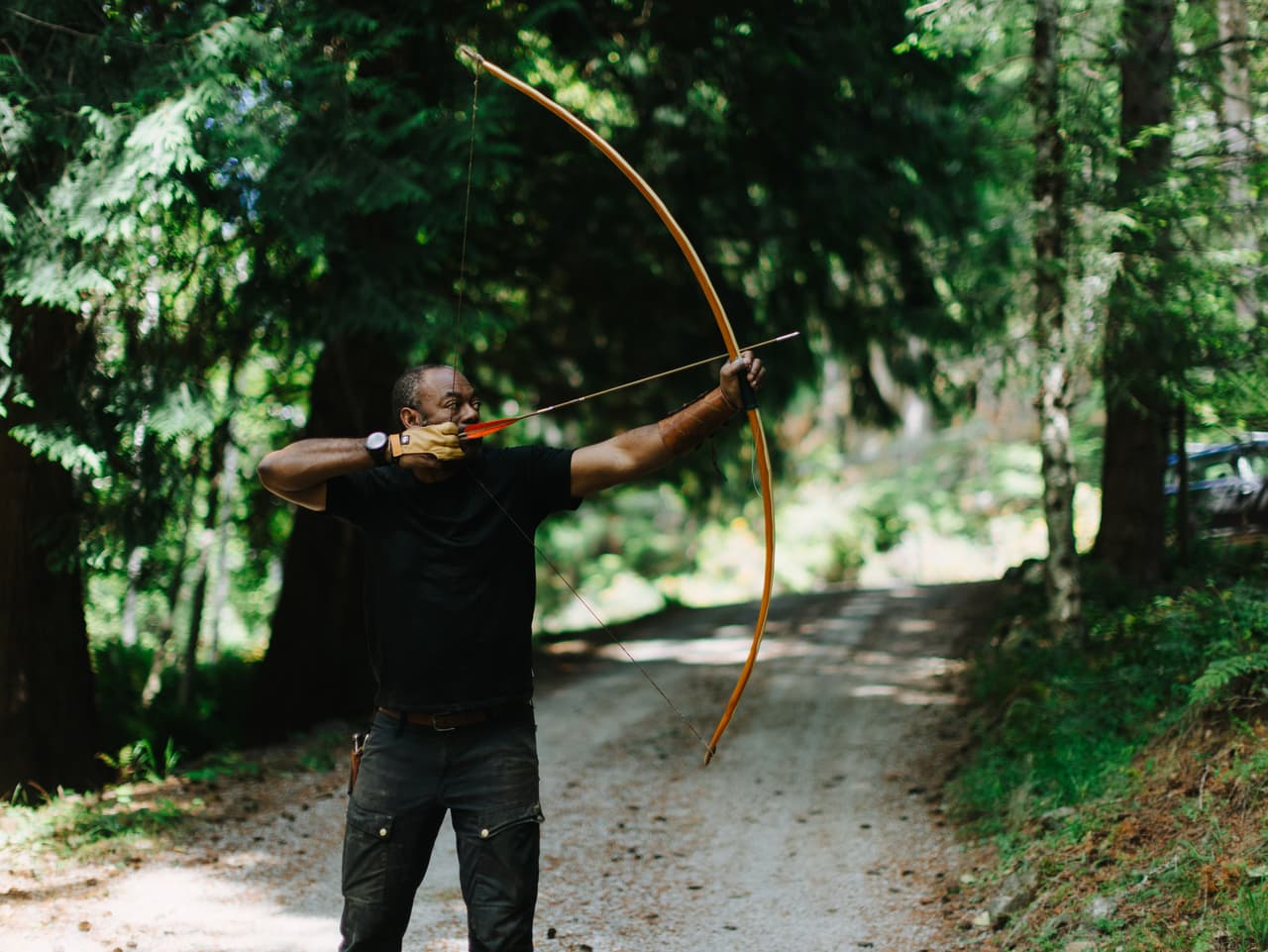 Christopher Applewhaite of Oshosi Handmade Bows drawing a wooden bow on a forest road