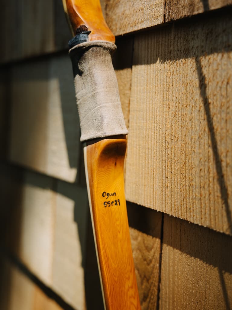 Leather-wrapped yew handle on one of the Oshosi handmade bows against cedar shingles