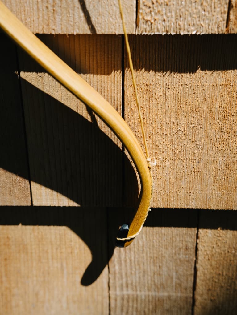 Curved tip of a recurve bow casting its shadow across cedar shingles