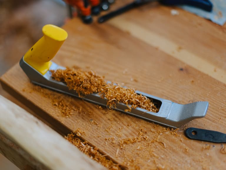 Spokeshave resting in fresh wood shavings on the workbench