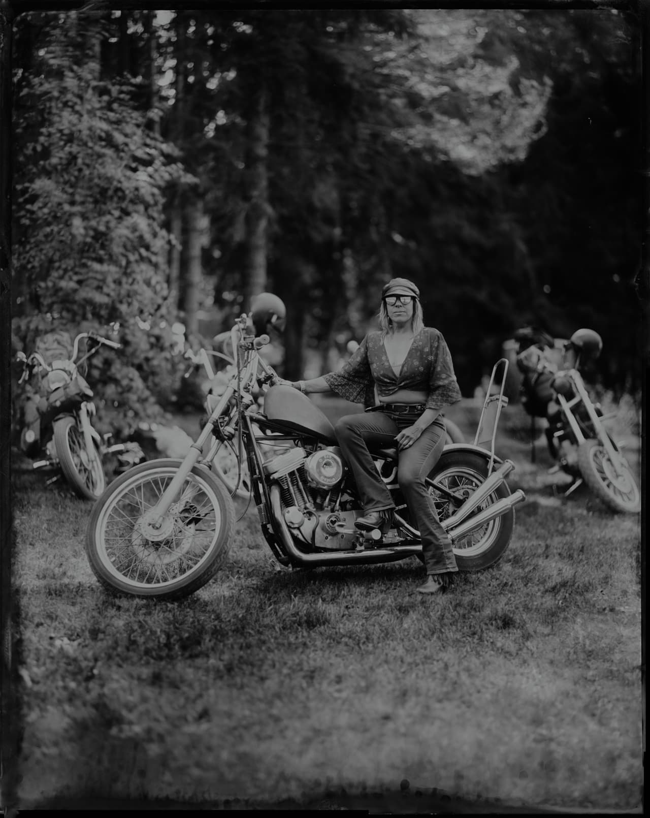 Two people sit on a motorcycle at Renegade Riot, trees blurred in soft focus behind