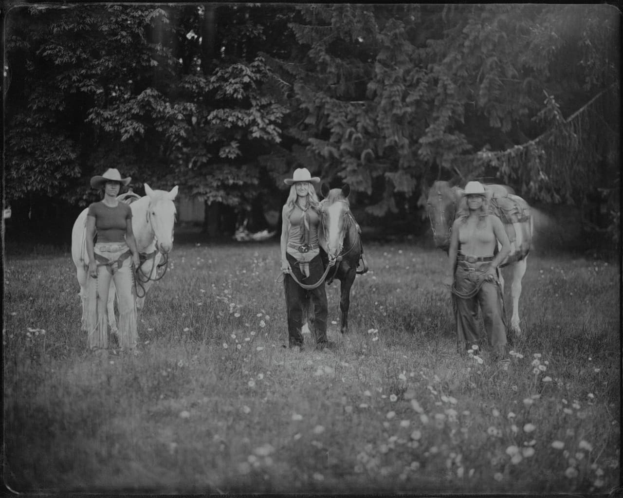 Cowgirl in hat holds coiled rope while standing with horse in meadow at Squamish River Ranch, evergreen forest behind